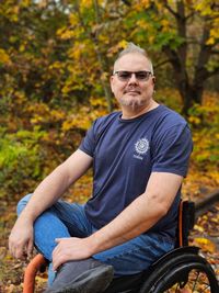 Portraitfoto von Christian im Rollstuhl vor herbstlichen Bäumen.