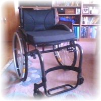 Foto eines nagelneuen Rollstuhls der im Wohnzimmer steht. Blickwinkel 1