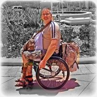Foto eines Mannes im Rollstuhl der vollgepackt mit EInkaufstüten ist. Ein voller Rucksack hängt an der Rückenlehne. Es ist ein Spaßbild, er lacht.